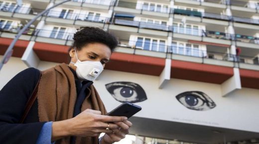 A young woman wearing a protective mask looks at her smartphone while passing by a grafitti representing two big watching eyes in Berlin, Germany on April 1, 2020. Illustrative Editorial (Photo by Emmanuele Contini/NurPhoto via Getty Images)
