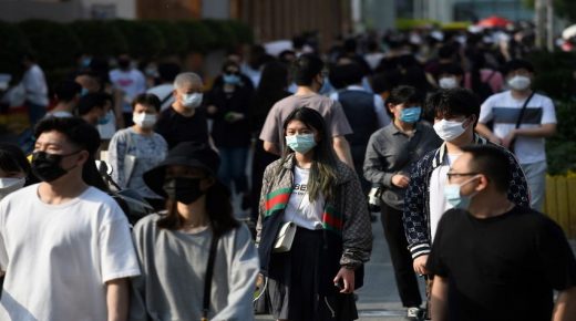 People wear face masks as a preventive measure against the COVID-19 coronavirus as they walk between shopping mall buildings in Beijing on May 2, 2020, the second day of a five-day national holiday. (Photo by GREG BAKER / AFP)