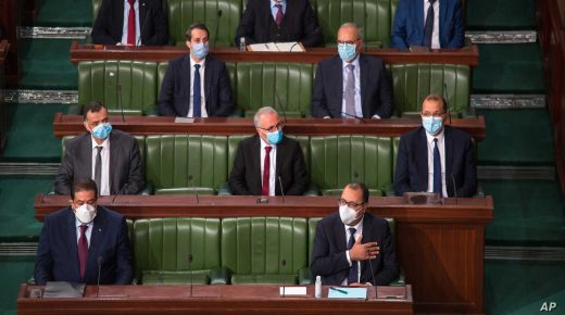 Tunisian Prime Minister Hichem Mechichi, first row at right, and designate Justice Minister Youssef Zouaghi, left first row, attend debates as the government faces a confidence vote, Tuesday, Jan.26, 2021 at the Parliament in Tunis. Tunisians are marching on their heavily guarded parliament Tuesday as lawmakers vote on a new government, after a week of youth protests and riots over poverty and lack of jobs that left one young demonstrator dead and hundreds jailed. Prime Minister Hichem Mechichi announced a government reshuffle last week in the midst of the unrest. (AP Photo/Hassene Dridi)