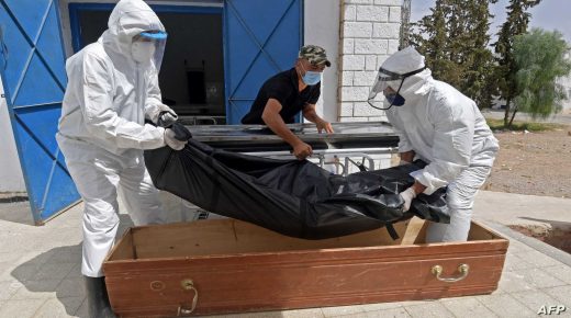 Tunisian municipality employees place the body of a COVID-19 victim into a casket at the Ibn al-Jazzar hospital in the east-central city of Kairouan on July 4, 2021. - Tunisia placed the capital Tunis and the northern town of Bizerte under a partial lockdown from until July 14 in a bid to rein in record daily coronavirus cases and deaths. (Photo by FETHI BELAID / AFP)
