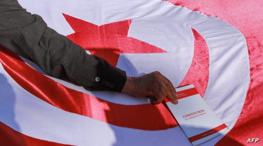 A man places a copy of the Tunisian constitution atop a Tunisian national flag during a demonstration called for by Tunisia's Islamist-inspired Ennahdha party against President Kais Saied's recent decrees, outside the Tunis Opera House in the centre of the capital Tunis on February 13, 2022. - Over a thousand demonstrators gathered in the centre of Tunis on February 13 a few hours after Saied replaced the Supreme Judicial Council (CSM), which he had dissolved a week prior, with another "temporary" body and gave himself the power to sack judges and prohibit their strikes. (Photo by ANIS MILI / AFP)