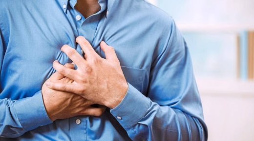 Mid-adult man clutching his chest in pain with a possible heart attack. He wears a blue, button down dress shirt. Heart disease.