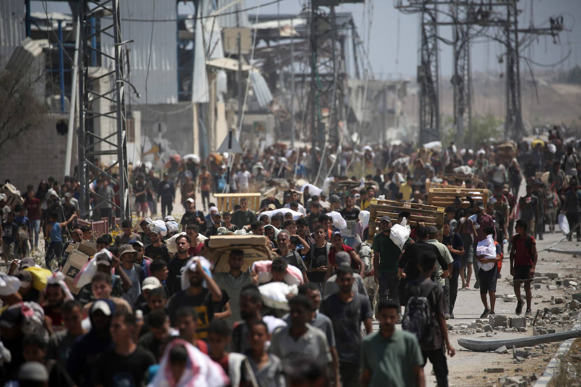 TOPSHOT - Palestinians return to the Nuseirat refugee camp from a US-backed Gaza Humanitarian Foundation distribution point near the Netsarim corridor in the central Gaza Strip, some carrying food parcels and others wooden pallets for burning, on July 27, 2025. (Photo by Eyad BABA / AFP)
