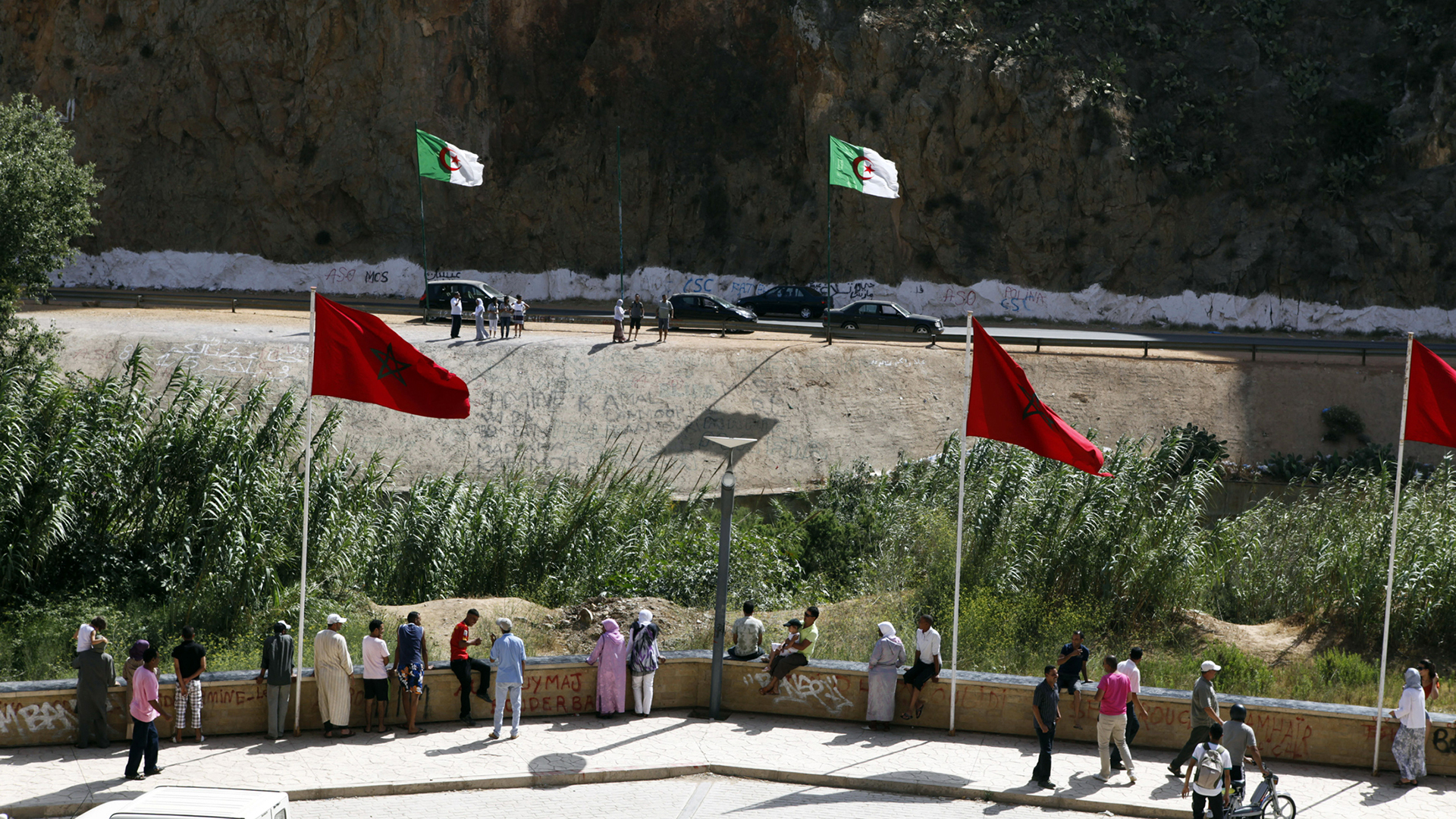 People stand near a border post on the Algerian side of the Morocco-Algeria border in the north east of Morocco July 31, 2011. Morocco's King Mohammed renewed calls on Saturday to normalise ties and reopen borders with wealthier neighbour Algeria, saying that Rabat wants to build an integrated North African economic bloc. Morocco closed the border following a 1994 Islamist militant attack in Marrakesh, which it blamed on Algeria's secret service, and the border region remains tense. REUTERS/Youssef Boudlal (MOROCCO - Tags: POLITICS)